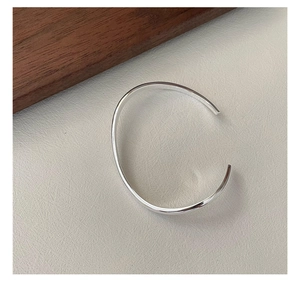 Close-up of a minimalist silver open bangle on a textured grey background with wood decor