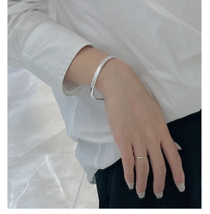 Close-up of minimalist wave-shaped S925 sterling silver bracelet and thin ring on wrist
