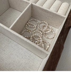 Detail of freshwater pearl elastic rings arranged in a beige linen jewelry organizer
