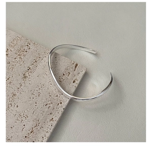Detail of minimalist S925 sterling silver curved bangle on natural travertine stone