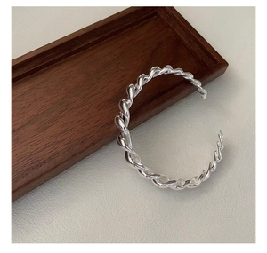 Vue détaillée du bracelet jonc torsadé en argent S925 poli sur un plateau en bois