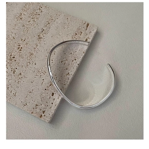 Close-up of minimalist S925 sterling silver wavy open bangle on a stone texture background