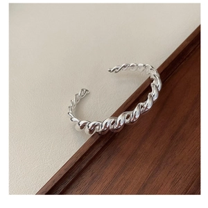 Gros plan d'un bracelet torsadé en argent S925 sur un plateau en bois épuré