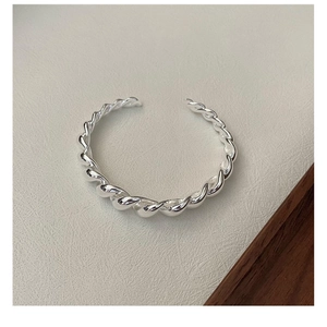 Vue détaillée d'un bracelet torsadé en argent sterling poli sur une texture cuir beige
