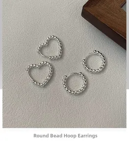 Detailed view of silver beaded hoop earrings in circular and heart shapes on textured surface