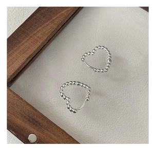 Macro detail of S925 sterling silver beaded heart earrings on minimalist wood glass