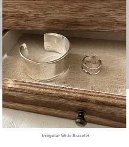 Detalle de conjunto de brazalete ancho y anillo de plata S925 sobre textura de lino
