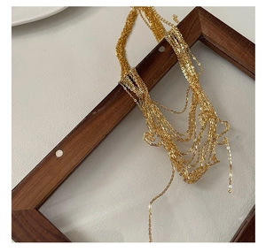 Macro detail of layered gold tassel necklace draped on a natural wooden frame