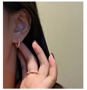 Detail of silver beaded hoop earring and pearl ring worn for a minimalist style