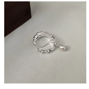 Macro shot of S925 sterling silver ring with textured waves and a hanging pearl pendant