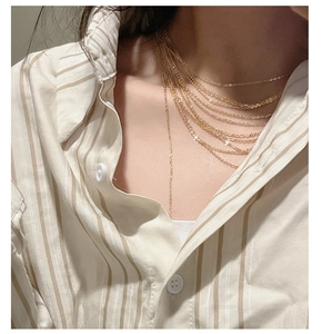 Detail of layered gold-tone tassel chains on a model wearing a striped shirt