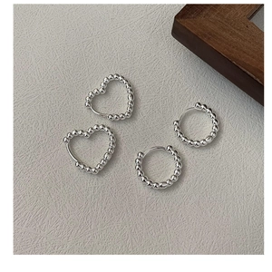 Detailed macro view of S925 silver beaded heart and round hoop earrings on gray cloth