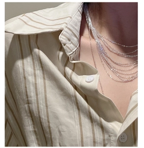 Detail of layered S925 sterling silver tassel necklaces worn by a model on a striped shirt