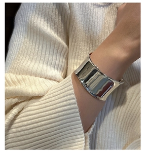 Primer plano de un brazalete ancho de plata S925 con diseño de ondas metálicas fluidas