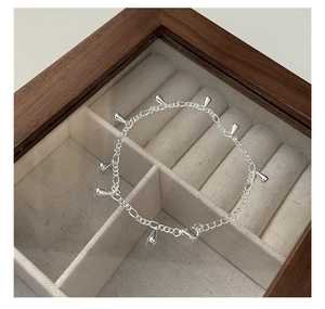 Detail of silver drop tassel bracelet with minimalist charms on a soft velvet display