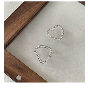 Detail shot of heart-shaped silver earrings crafted with delicate small round beads