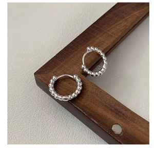 Detail shot of silver bead textured hoop earrings on a warm wooden frame backdrop