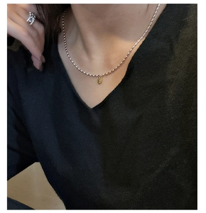 Détail d'un collier de perles argentées avec pendentif ovale doré sur haut noir