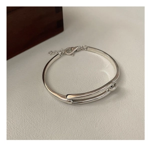 Detail of S925 silver geometric bangle with lobster clasp on a beige leather background
