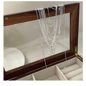 Detailed view of multiple silver layered chains draped over a wooden jewelry box