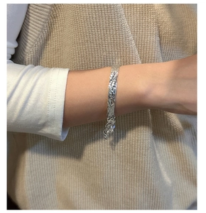 Macro view of wide hammered texture on a silver bangle with delicate chain detail