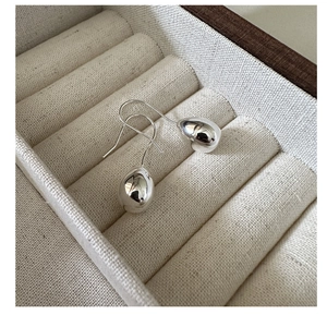 Close-up of polished S925 sterling silver teardrop earrings on a beige fabric background