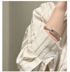 Detail of interlocking S925 silver geometric bangle on a striped shirt sleeve