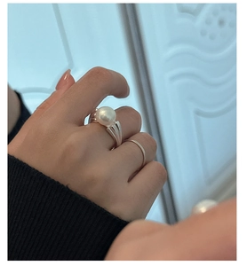 Close-up of a large white pearl ring with silver ribbed band worn on a finger