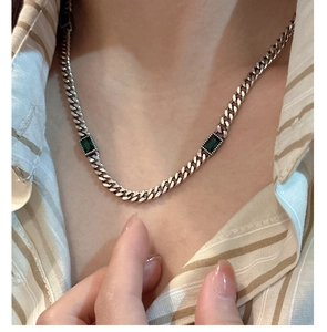 Detail of silver Cuban chain necklace with green emerald-cut stones on a model