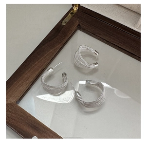 Detailed view of silver minimalist woven hoop earrings and ear cuff on a glass case