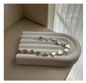 Close-up of matte silver heart-shaped bracelet links on a minimalist stone display stand
