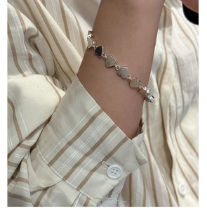 Detail of S925 sterling silver heart-shaped bracelet on wrist with striped shirt