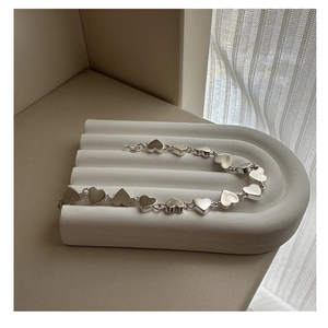 Detail of matte silver heart-link bracelet on a white textured minimalist stand