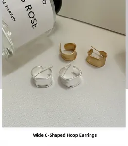 Flat lay of wide C-shaped earrings in gold and silver with a matte brushed texture finish