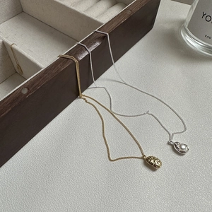 Detailed shot of S925 silver pearl pea necklace and golden oval pendant on a jewelry box