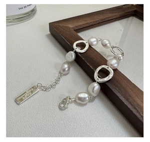 Detailed close-up of Baroque pearl and silver link bracelet with engraved metal tag