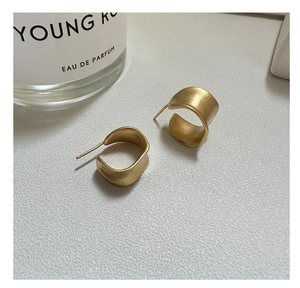 Detailed shot of gold matte C-shaped earrings with a brushed texture on a neutral surface