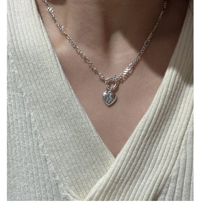 Detail of silver heart pendant with star engraving worn over a cream knit sweater