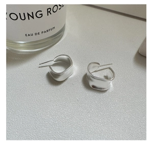 Macro shot of matte silver minimalist C-shaped wavy earrings on a textured grey stone surface