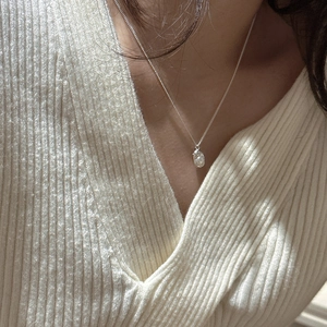 Detailed view of S925 sterling silver pea necklace with white pearl on a beige knit sweater