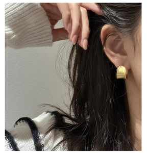 Close-up of minimalist gold matte C-shaped earrings worn by a model in white knitwear