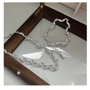 Detail of twisted silver necklace and bracelet set on a luxury wooden jewelry display case
