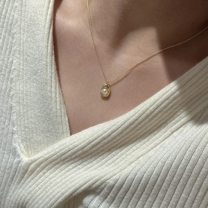 Detail of a gold pea pendant necklace with a white pearl on a model wearing a white sweater