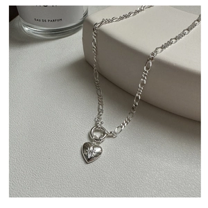 Macro detail of S925 silver Figaro chain necklace with star-engraved heart pendant