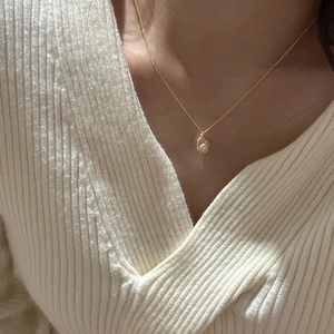 Detail of a minimalist gold pea pendant with white pearl on a delicate silver chain