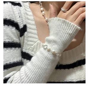 Detail view of pearl necklace, bracelet and silver ring on a striped knit sweater