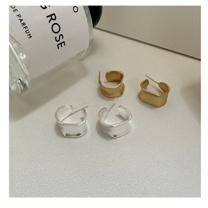 Macro shot of matte gold and silver C-shape wavy earrings on a soft cream background