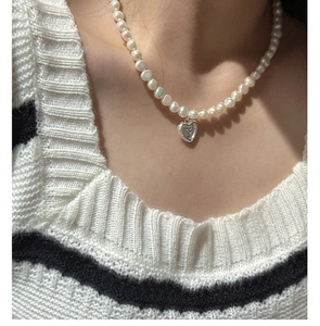 Détail d'un pendentif cœur en argent S925 sur collier de perles avec pull rayé