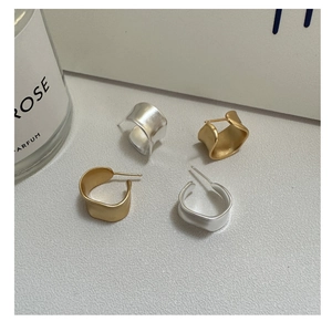 Close-up of matte gold and silver irregular C-shaped earrings on a textured surface