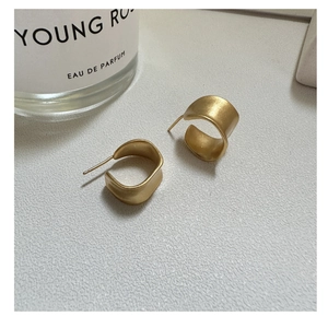 Close-up of matte gold C-shaped earrings with brushed texture on white surface